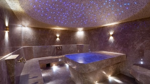A modern bathroom with a large bathtub, marble walls, and a ceiling with embedded lights.