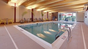 An indoor swimming pool with a wooden ceiling and tiled floor, surrounded by yellow chairs and potted plants. - Home2 Suites BY Hilton Hagerstown (Hagerstown)