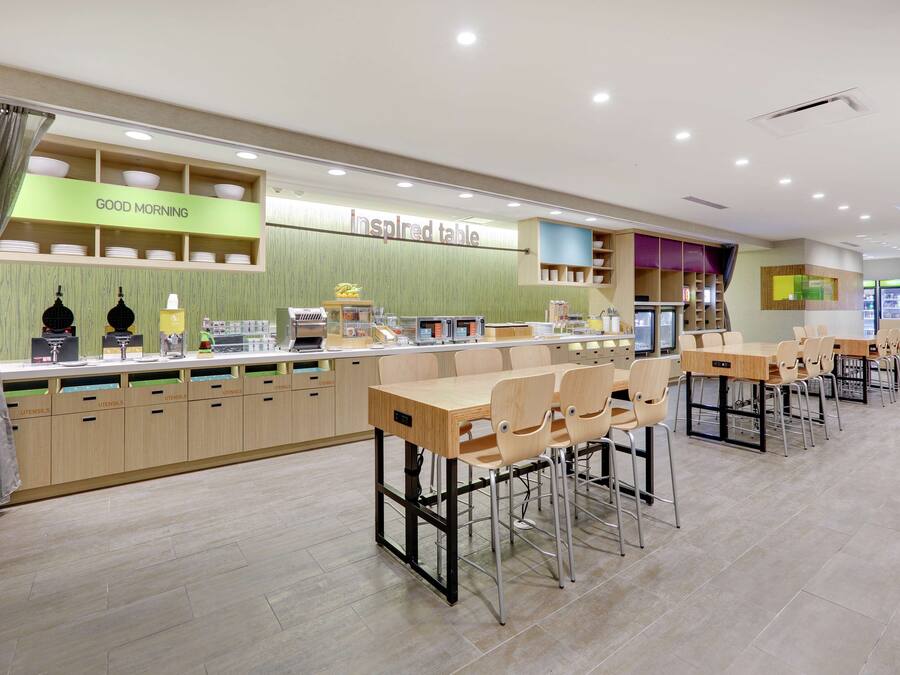 Une cafétéria moderne avec un panneau indiquant « Bonjour », un comptoir intitulé « Espace d’inspiration » et plusieurs coins repas avec des tables et des chaises.
