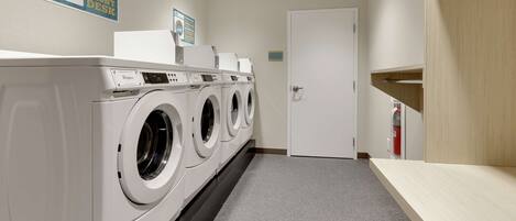 A laundry room with a front-loading washer and dryer, a wooden bench, and a door.