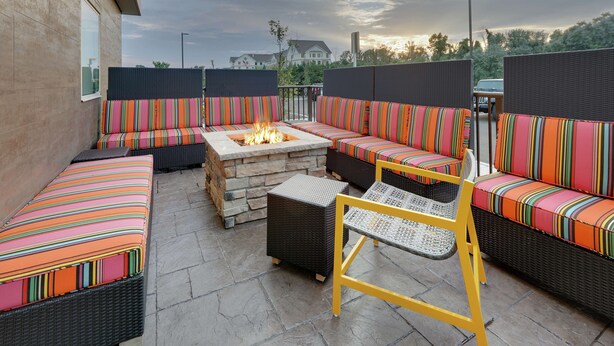 An outdoor patio with wicker furniture, a stone fire pit, and a view of the surrounding neighborhood. - Home2 Suites BY Hilton Hagerstown (Hagerstown)