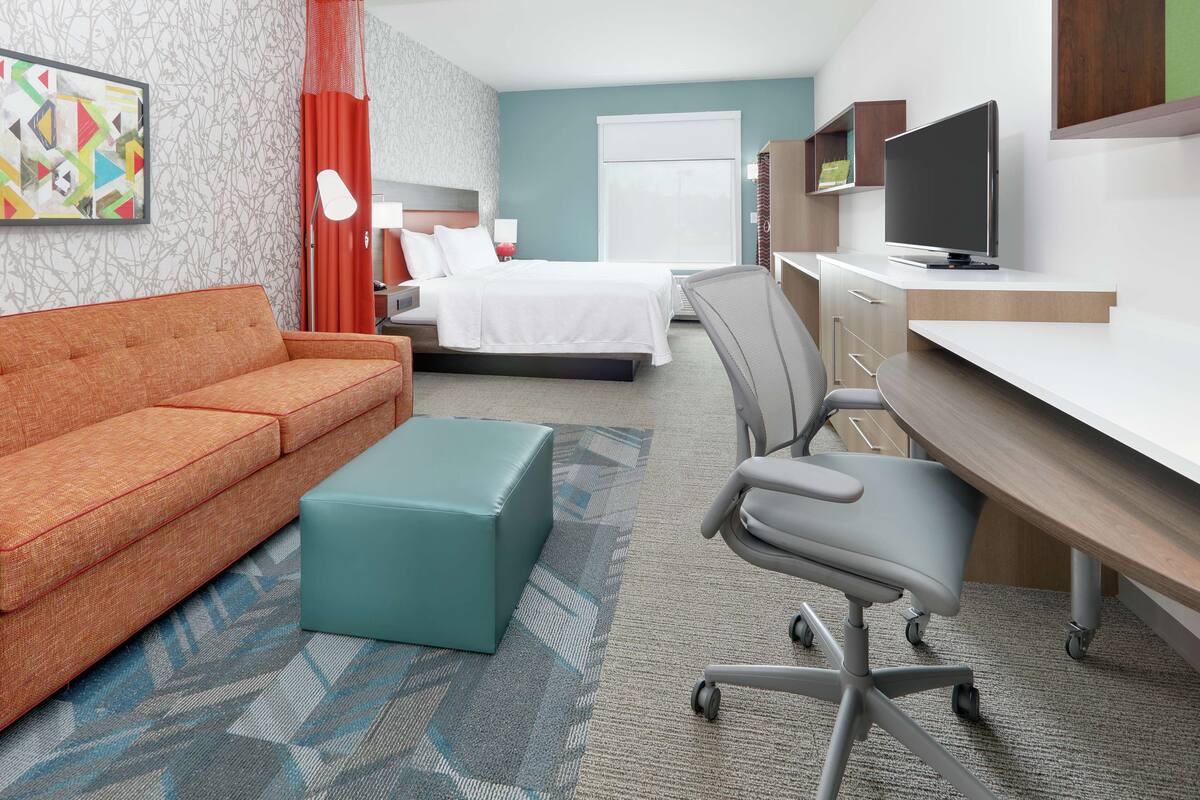 A hotel room with a bed, a sofa, a desk, a chair, and a television.