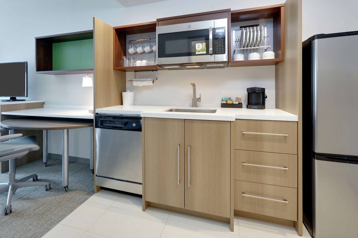 A modern kitchen with a dishwasher, microwave, and refrigerator. There is a wooden cabinet with drawers and a countertop with a coffee maker.
