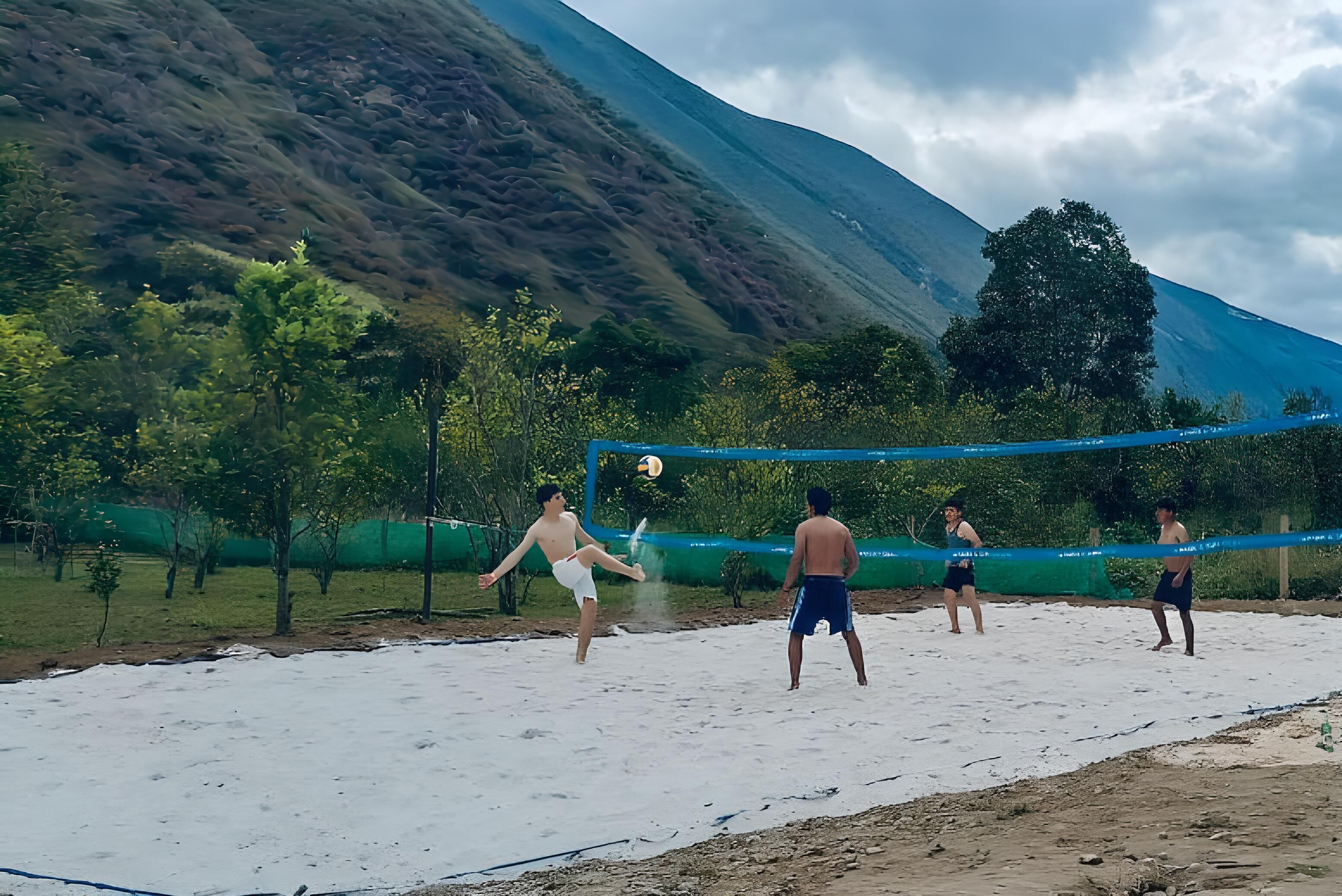 Partido de voleibol en una cancha de arena con montañas al fondo.