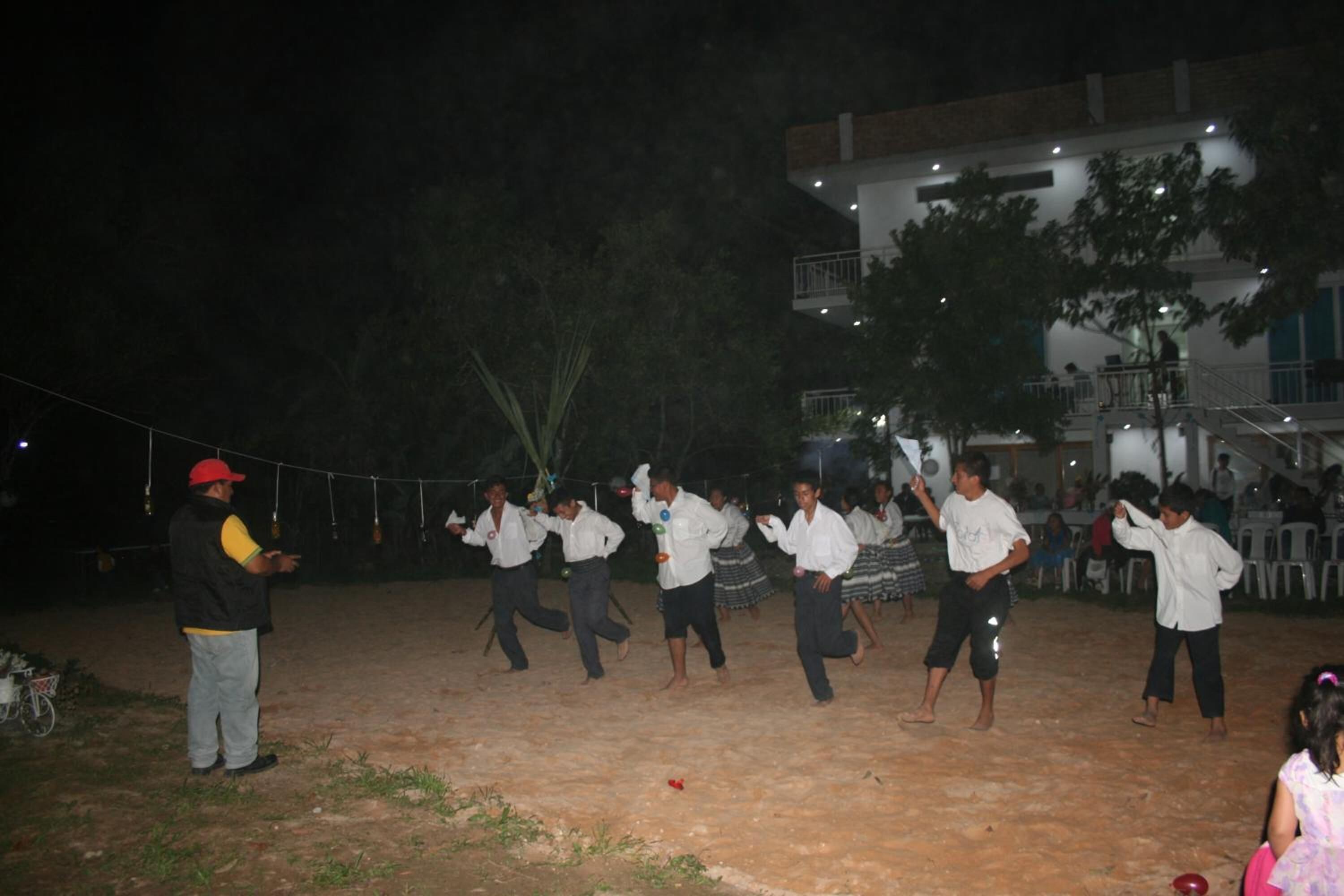 A group of people performing a dance in an outdoor area with a building in the background.