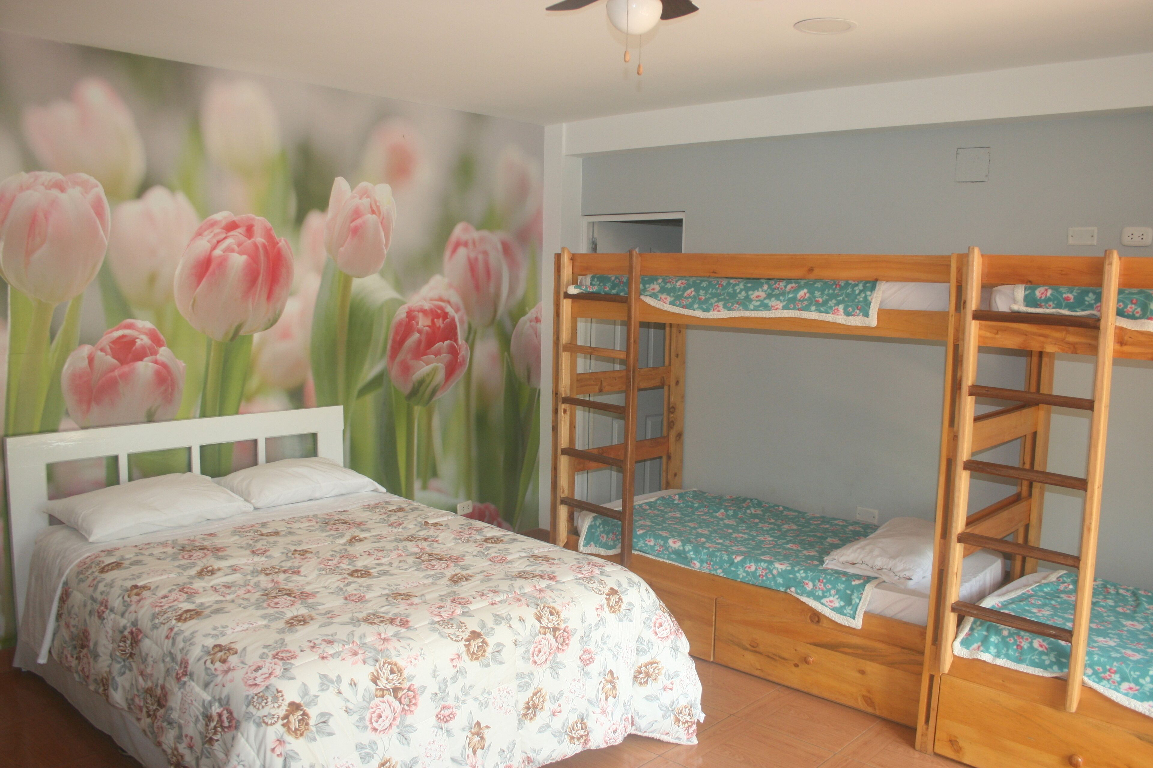 A bedroom with a bunk bed, a single bed, floral wallpaper, and a ceiling fan.