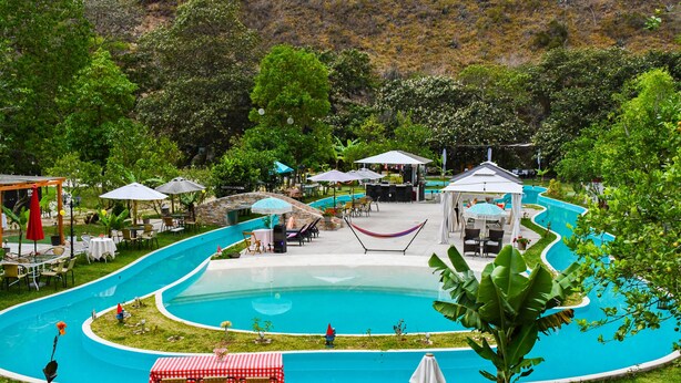 A pool area with a winding pool design, surrounded by lush greenery and shaded seating areas. - Zoila's Suite Escape (Tingo)