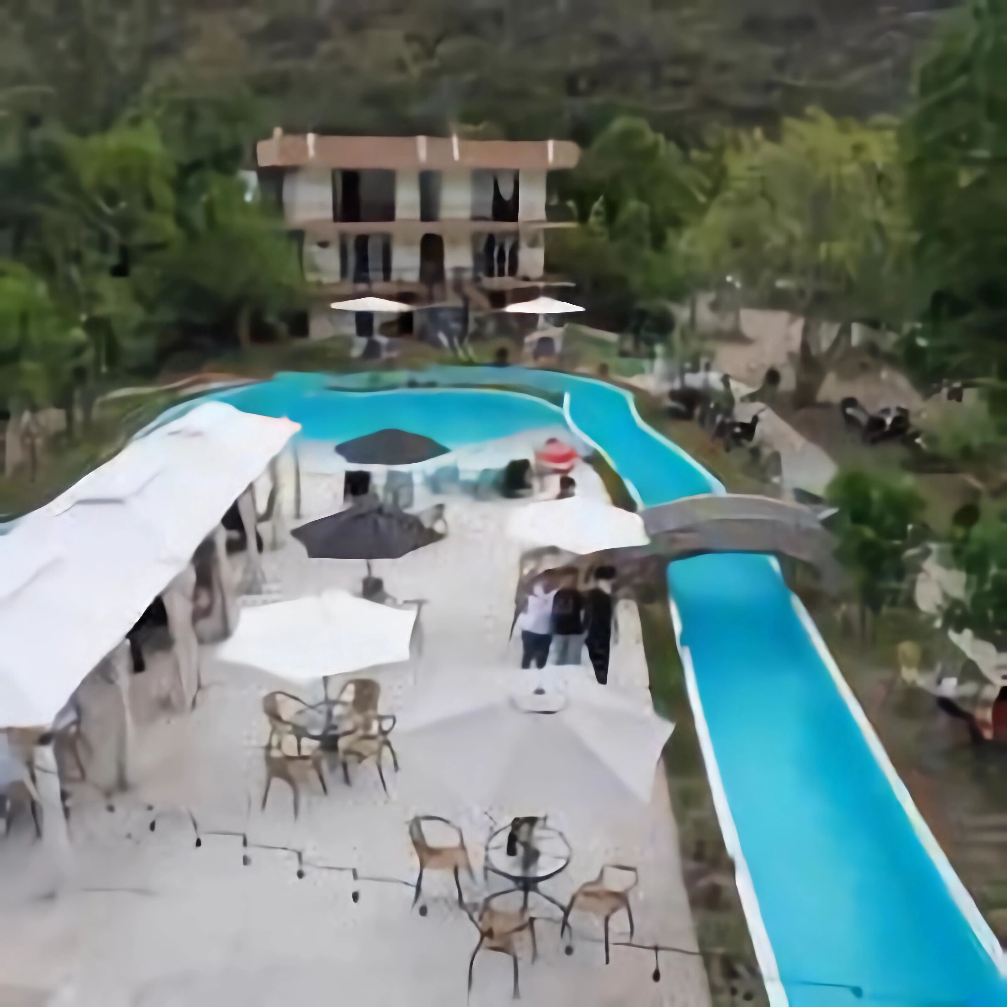A pool area with outdoor seating and umbrellas, surrounded by greenery.