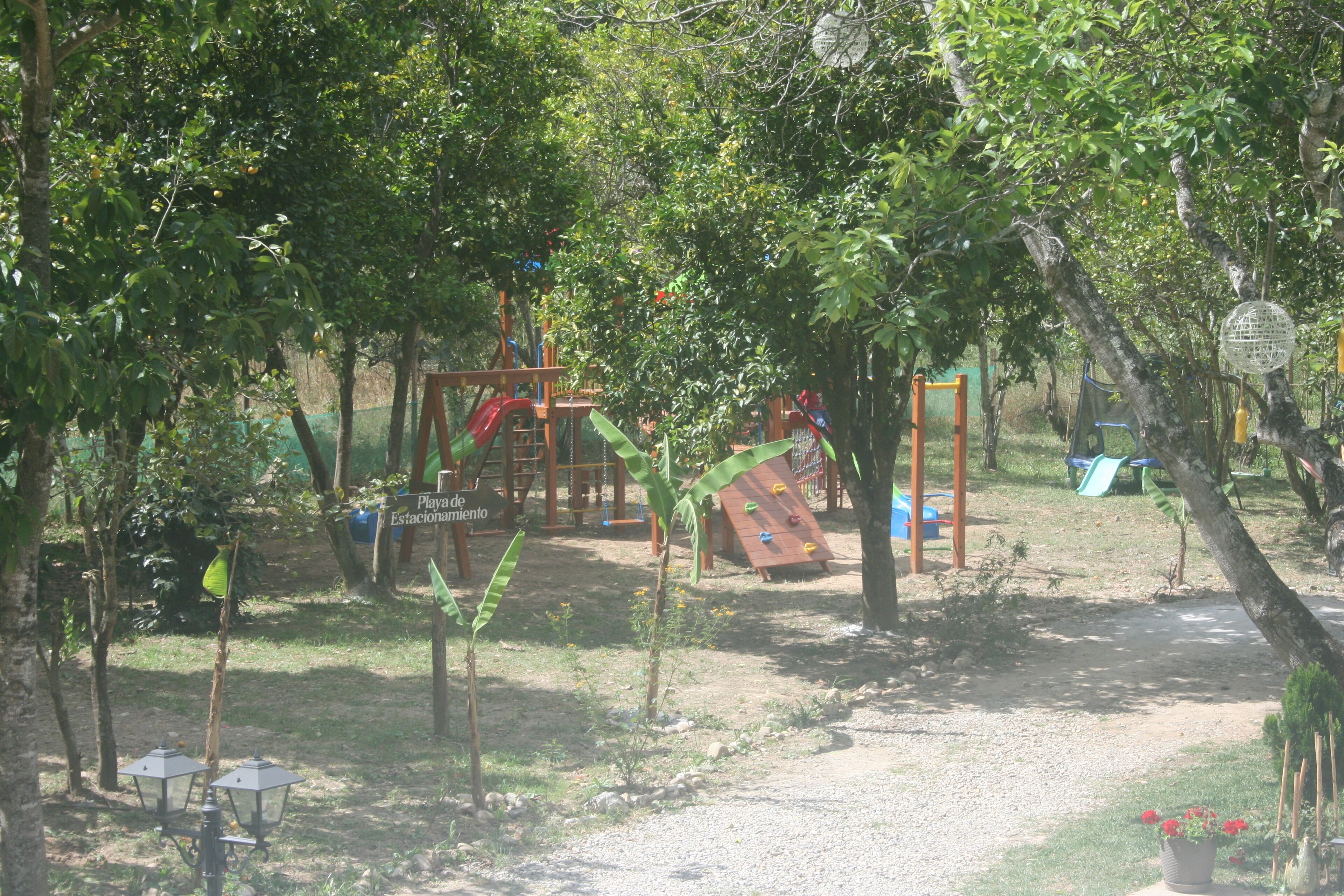 Un parque infantil con diversas estructuras de juego, rodeado de árboles y un sendero de tierra.