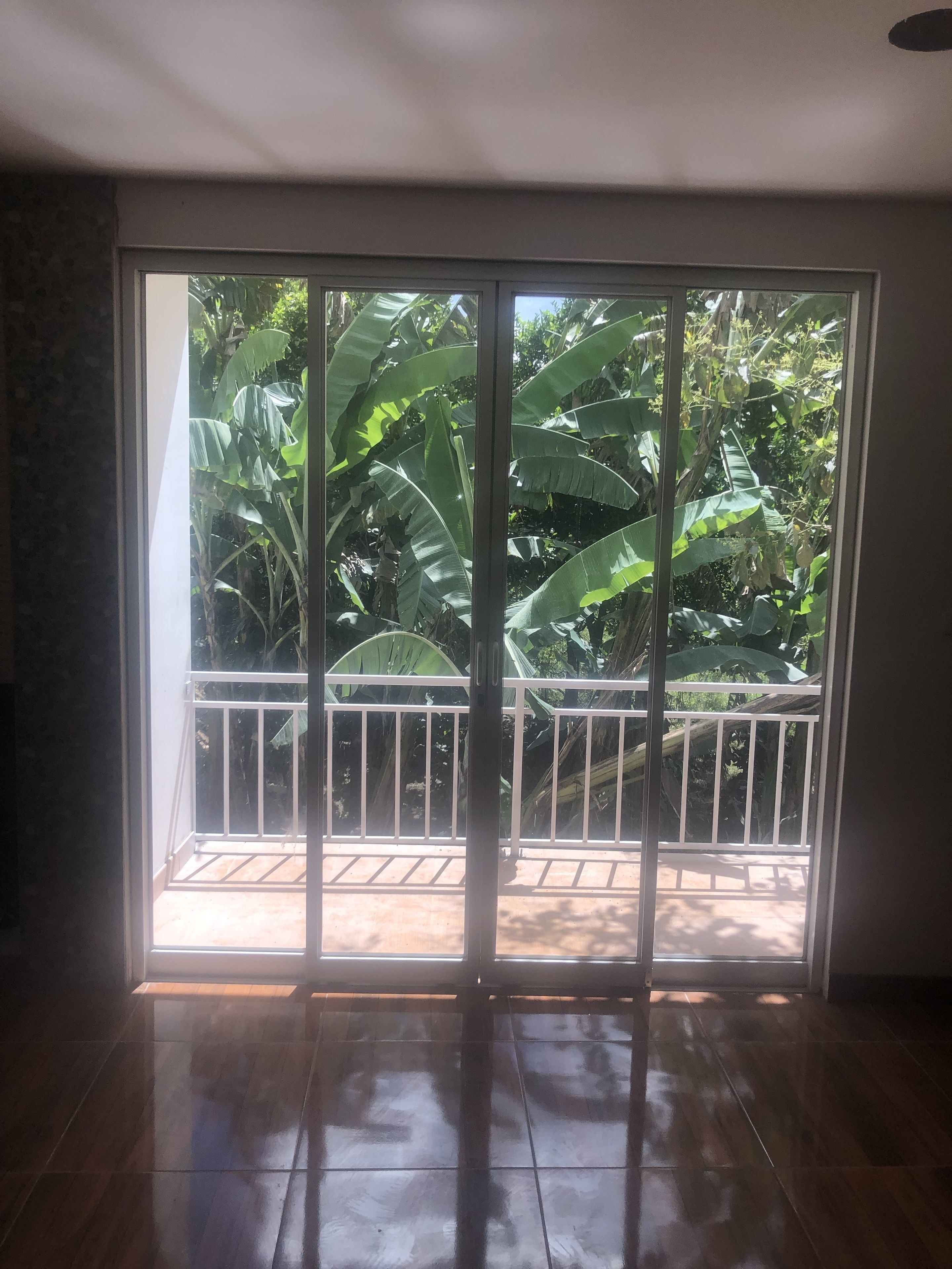 A room with a sliding glass door leading to a balcony with a white railing.