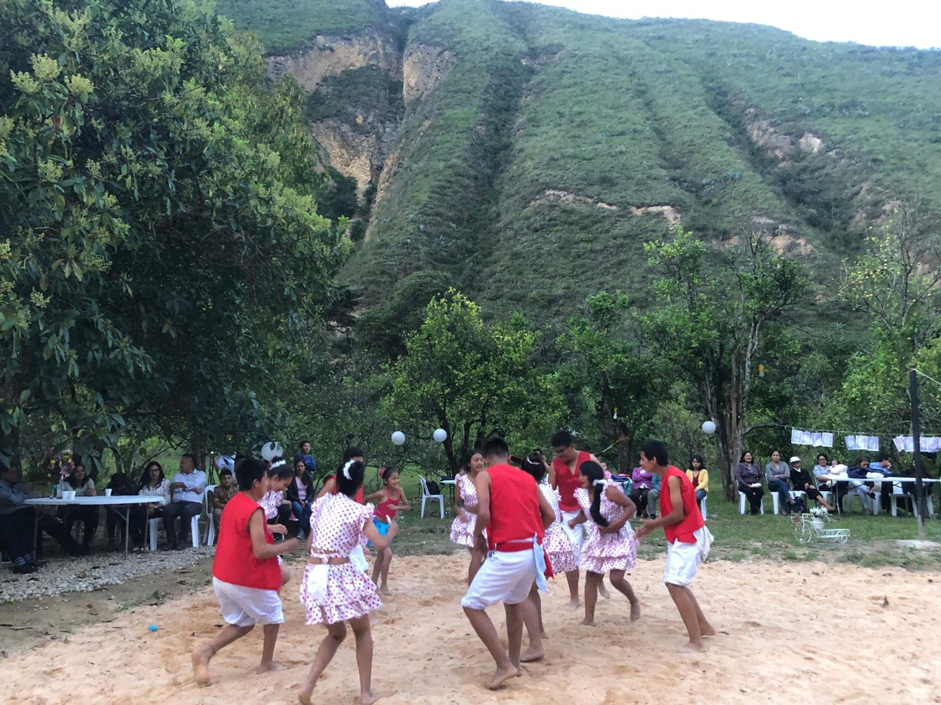 A group of people dancing in a sandy area with a mountainous backdrop.