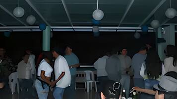 A covered outdoor seating area with tables and chairs, a ceiling with hanging lights, and a dark background.