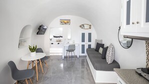 A compact living space with a dining area, a sofa, a small table, and a kitchen area. - White Side Suites (Santorini)