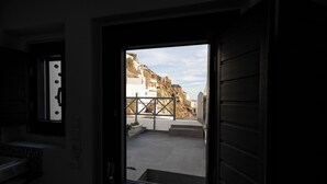 A view from a room with a large window, revealing a courtyard with steps leading to a white building on a hillside. - White Side Suites (Santorini)