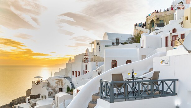 A coastal hotel with white buildings, a balcony with wicker furniture, and a sunset view. - White Side Suites (Santorini)