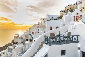 A coastal hotel with white buildings, a balcony with wicker furniture, and a sunset view. - White Side Suites (Santorini)