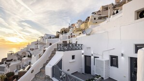 A white-washed building with a staircase leading to a balcony overlooking the sea. - White Side Suites (Santorini)