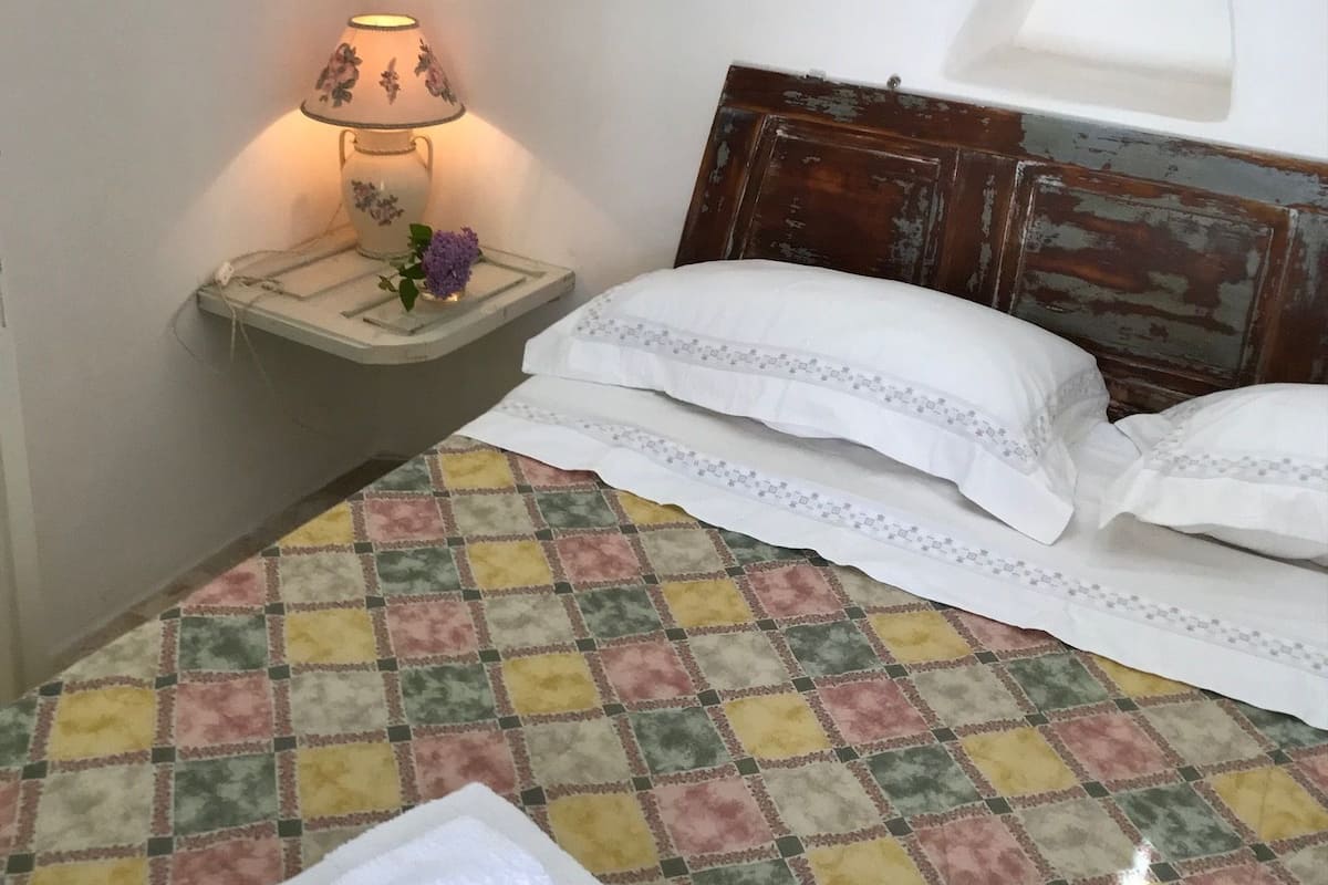 A neatly made bed with a quilt, pillows, and a folded towel on a checkered floor.