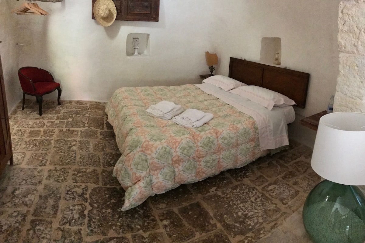 A bedroom with a bed, a chair, a lamp, and a wall-mounted hat.