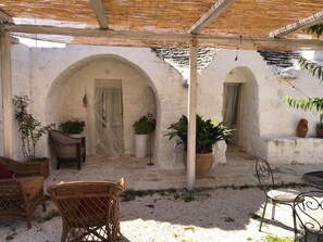 A covered outdoor seating area with wicker furniture, potted plants, and stone walls. - Borgo Trulli 1789 (Ostuni)