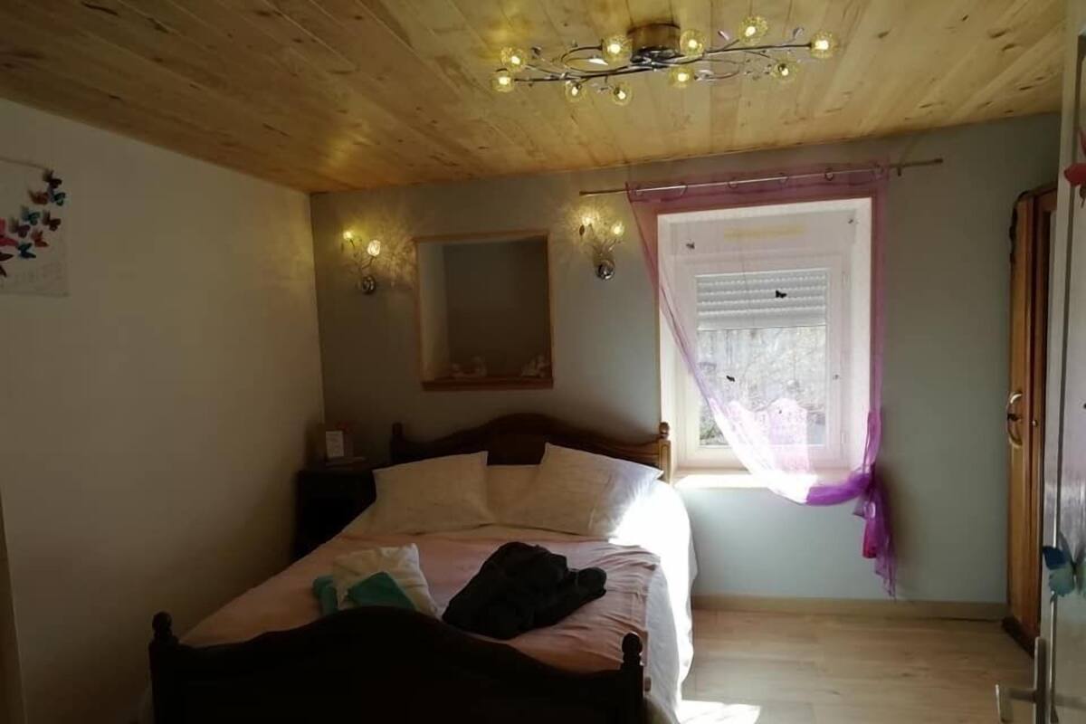 Un dormitorio con techo de madera, una cama con almohadas, una mesita de noche, una ventana con cortinas y un espejo en la pared.