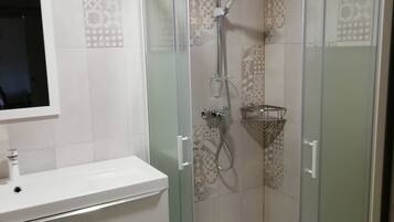 Un baño moderno con ducha envuelta en vidrio, un lavabo blanco y azulejos estampados.