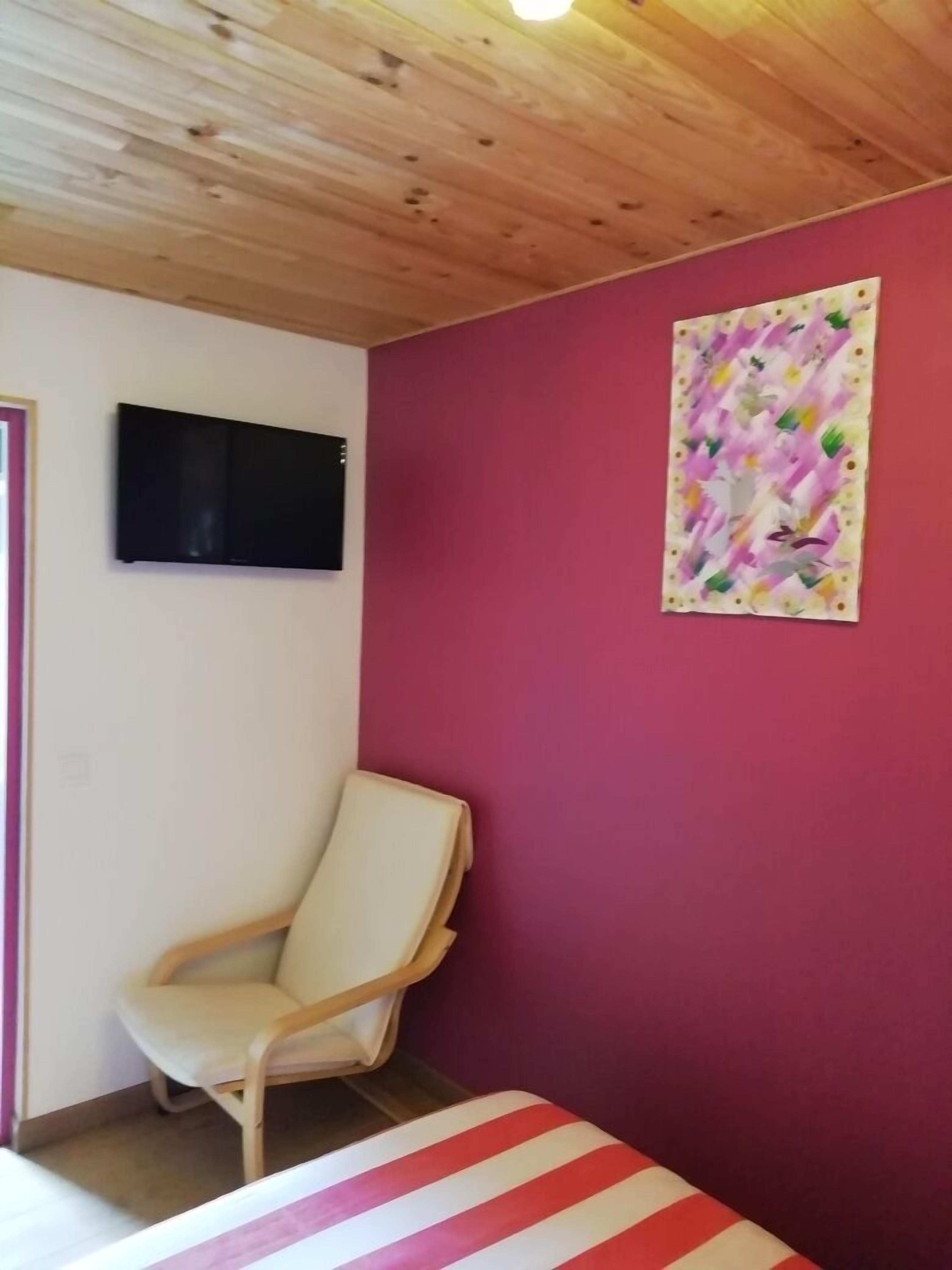 Een kamer met een houten plafond, een flatscreen televisie aan de muur, een beige stoel en een kleurrijk abstract schilderij.