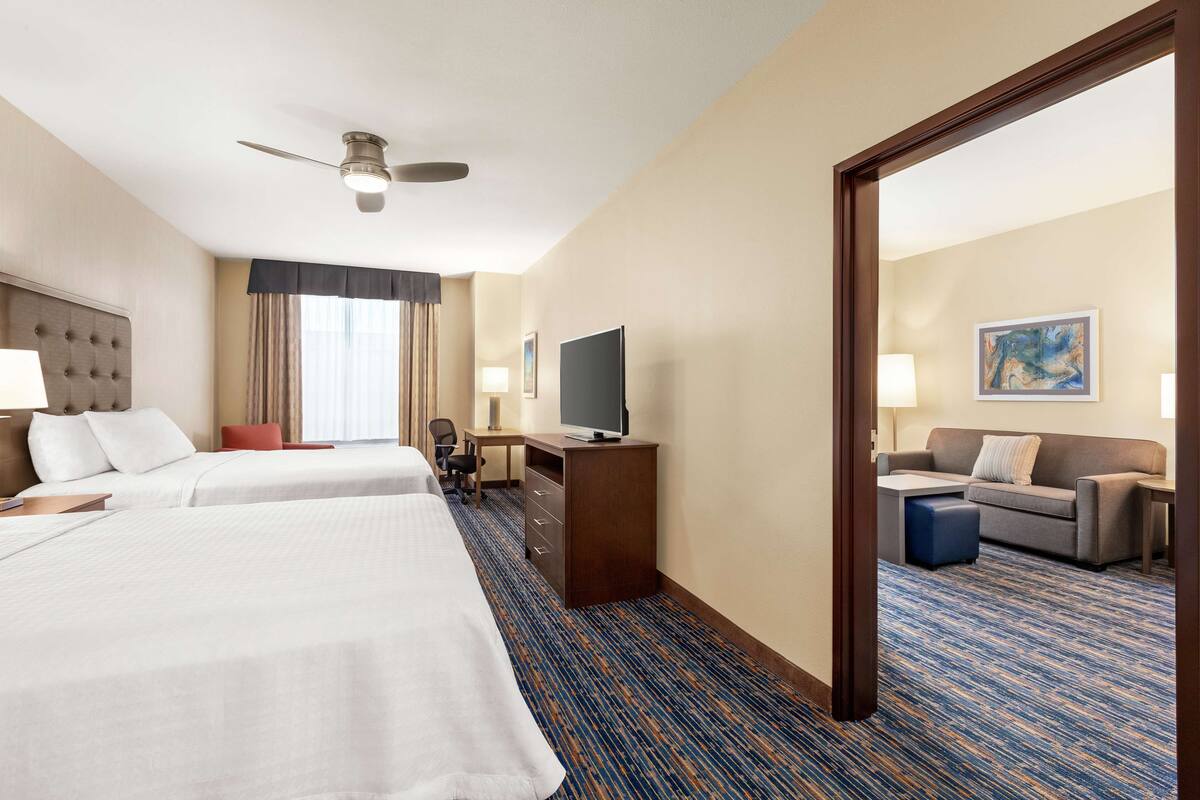 A hotel room with two beds, a desk with a TV, a sofa, and a large mirror.