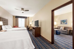 Habitación de hotel con dos camas, un escritorio con televisor, un sofá y un espejo grande.