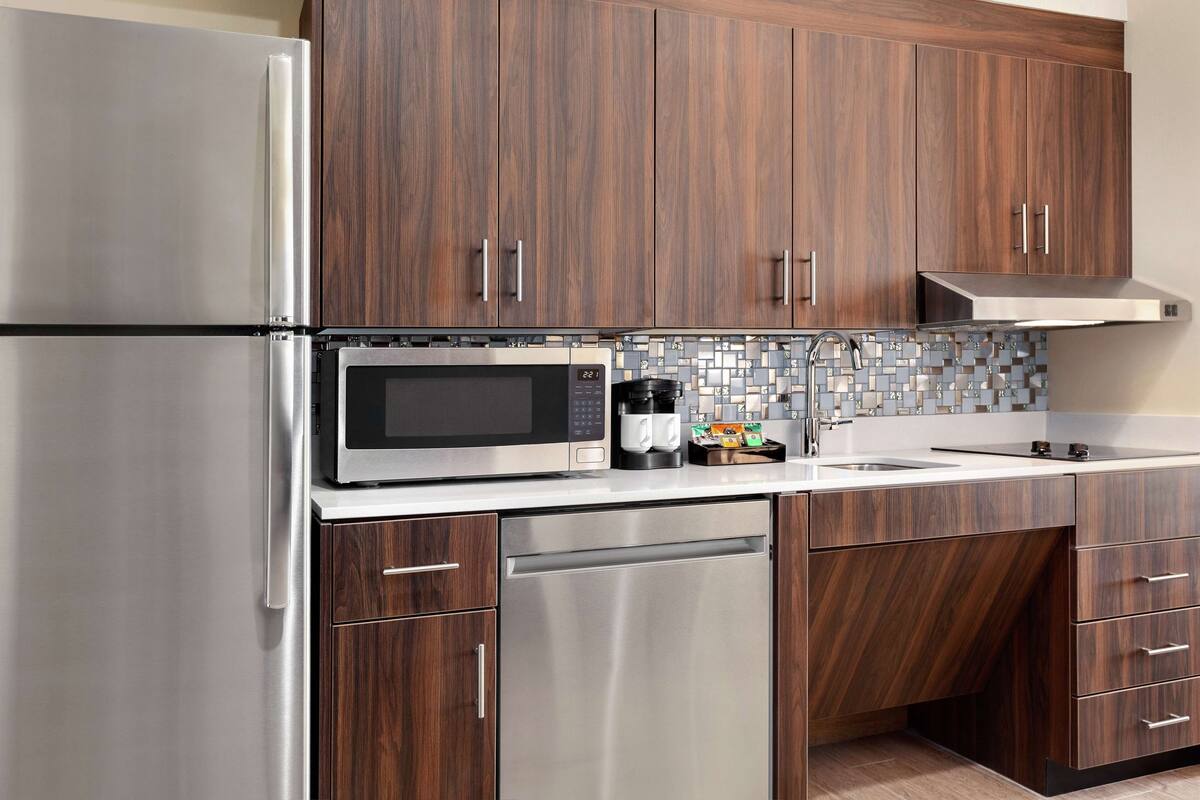 A modern kitchen with stainless steel appliances, wooden cabinets, and a tiled backsplash.