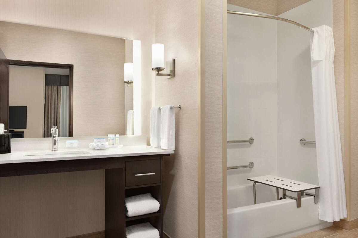 A modern bathroom with a sink, mirror, towel rack, and a shower area with a glass door.
