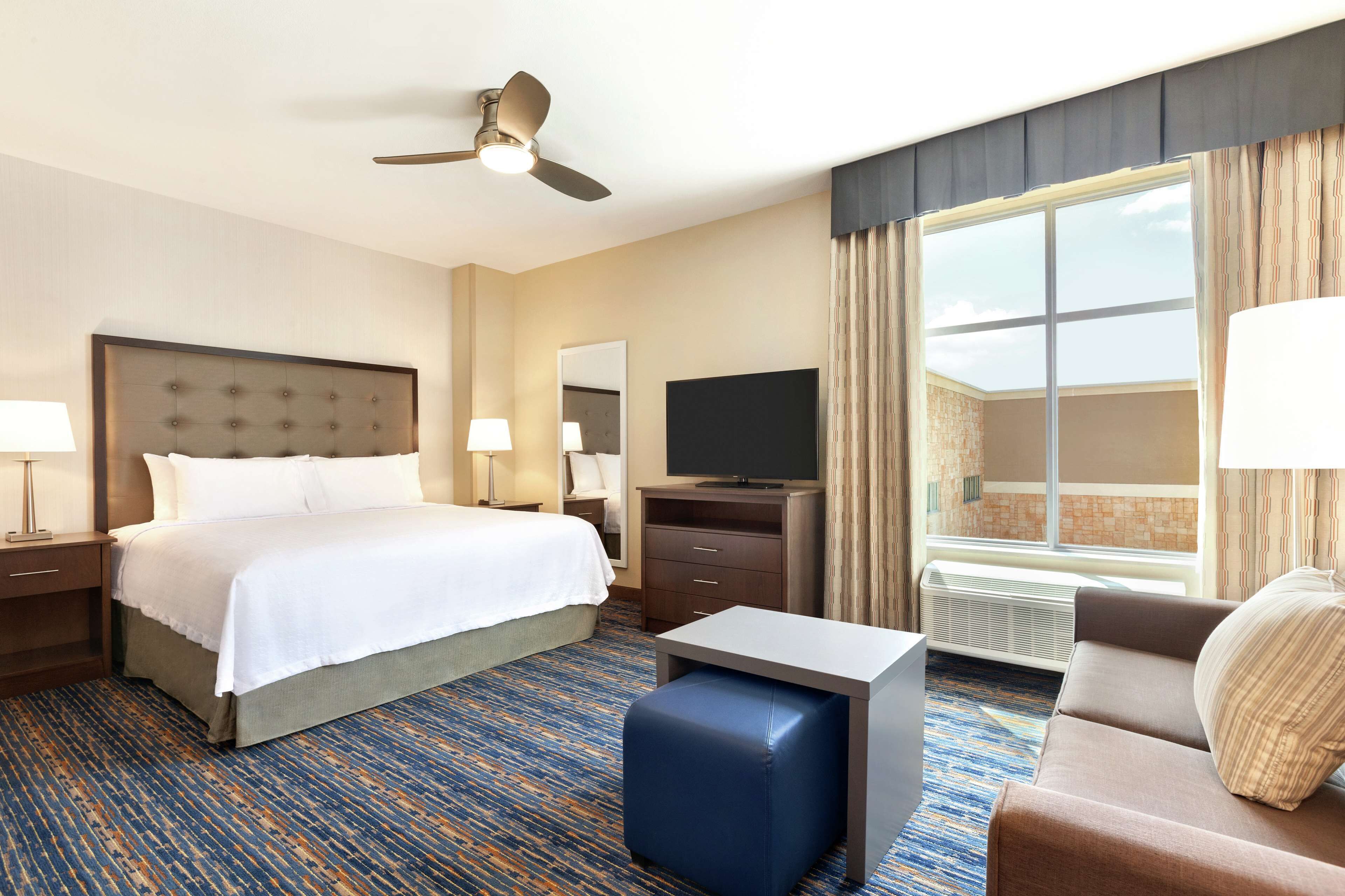 Una habitación de hotel con cama, escritorio, televisor y ventana con cortinas.