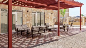 Un área de estar al aire libre con una pérgola, paredes de piedra y piso a cuadros.