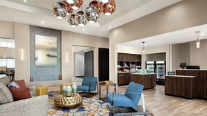 Un vestíbulo moderno de hotel con zona de estar, un cuadro grande, un minibar y una recepción.
