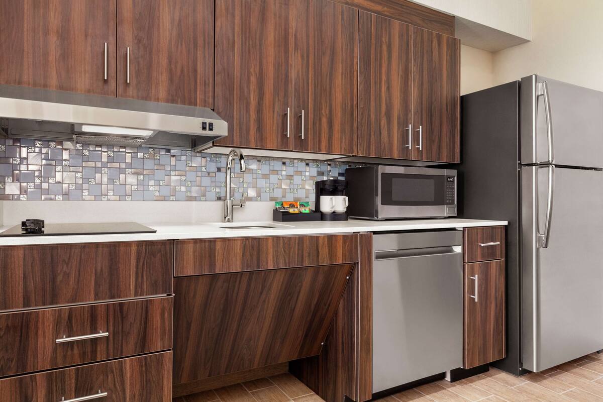 A modern kitchen with wooden cabinets, a stainless steel refrigerator, a microwave, and a dishwasher.