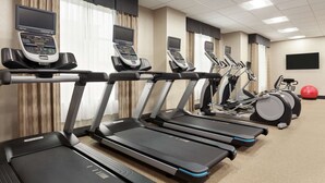 Un gimnasio con varias cintas de correr, bicicletas estáticas y una máquina de remo.