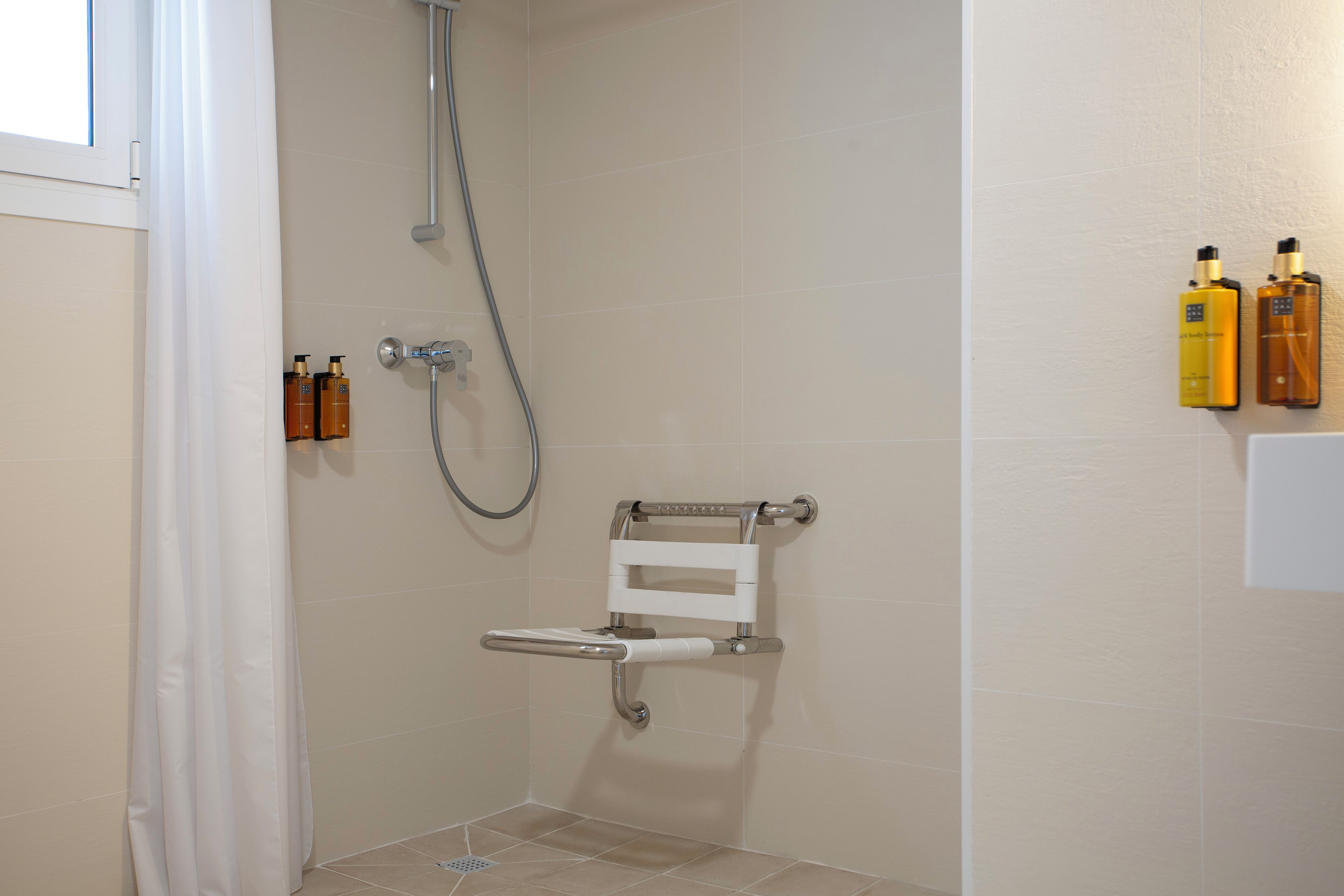 A shower area with a grab bar, a handheld showerhead, and toiletries on the wall.