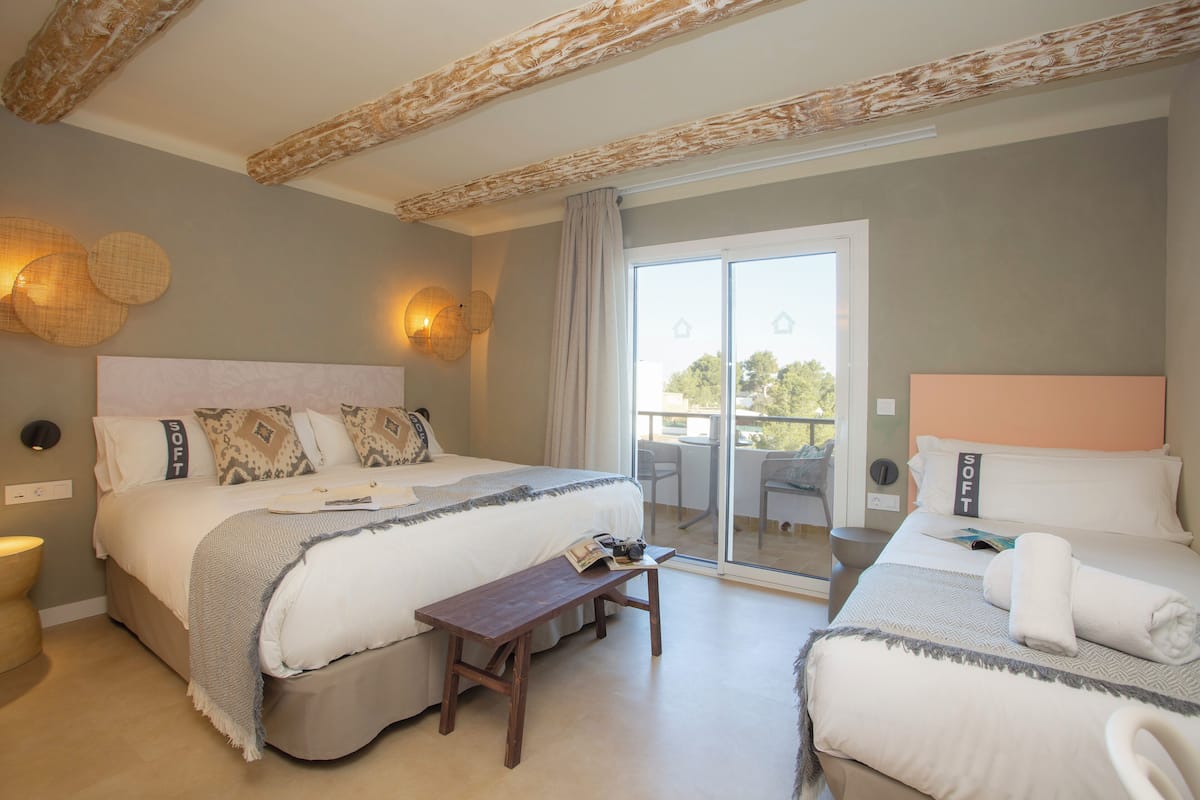 A hotel room with a large bed, a smaller bed, a bench, and a balcony with a view.