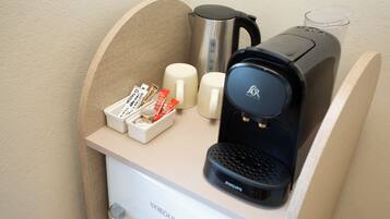 A compact kitchenette with a coffee maker, two mugs, a kettle, and a coffee pod holder.