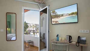 Ein Hotelzimmer mit Balkon, Schreibtisch mit Telefon, Kaffeemaschine und Fernseher, der eine Strandansicht zeigt.