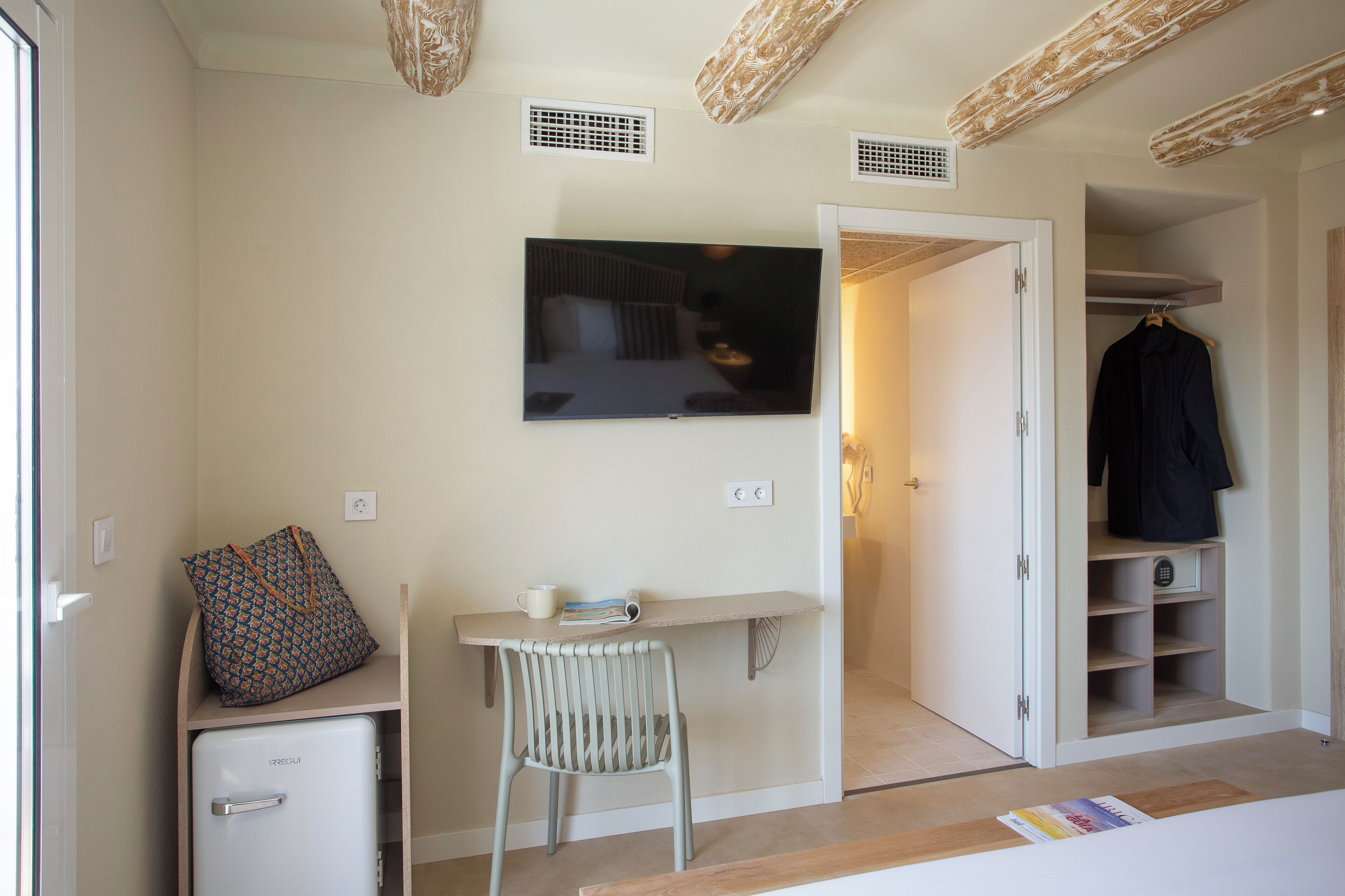 Une petite pièce comprenant un bureau, une chaise et un téléviseur fixé au mur.
