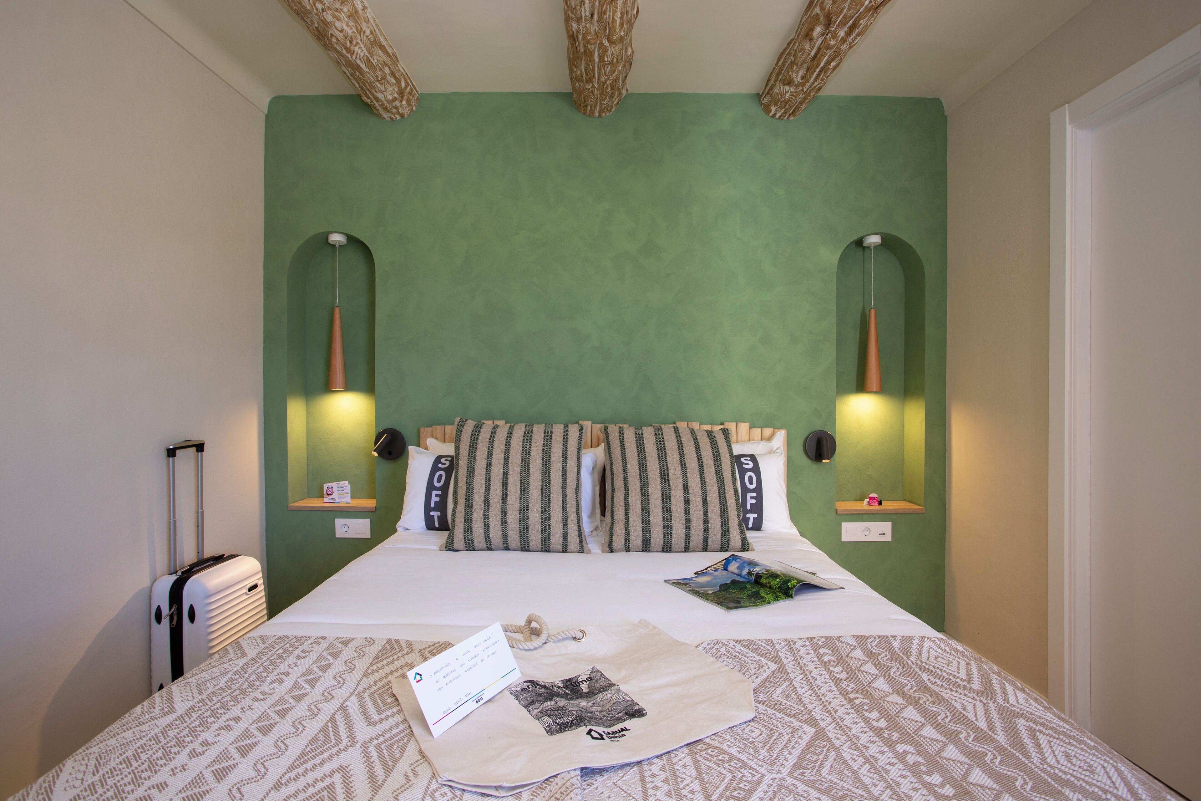 Una cama bien hecha con almohadillas a rayas, una maleta y una revista sobre la cama.