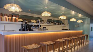 Eine Bar mit einer langen Theke, mehreren Hockern und hängenden Pendelleuchten.
