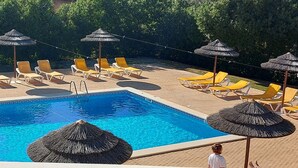 A pool area with sun loungers and thatched umbrellas.