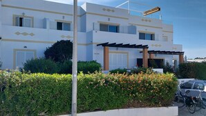 A modern building with a white facade, multiple windows with shutters, and a covered outdoor area.