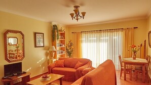 A living room with a sofa, a dining table with chairs, a TV, and a bookshelf.