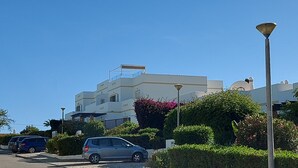 A modern building with a flat roof, a balcony, and a small dome structure. There are cars parked in front and a street lamp in the foreground.