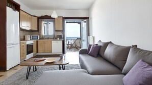 Un soggiorno moderno con un divano grigio e cuscini viola, un tavolino in legno e un angolo cottura con mobili in legno e un frigorifero bianco.