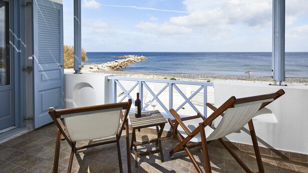 Una terrazza con vista sul mare, con un tavolo, una bottiglia, bicchieri, sedie di legno e una ringhiera bianca.