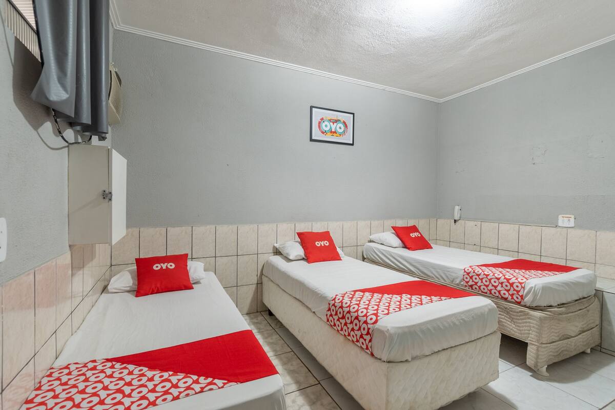 Ein Hotelzimmer mit drei Einzelbetten, jedes mit einem roten OYO-Branded Kissen und einer gemusterten Decke.